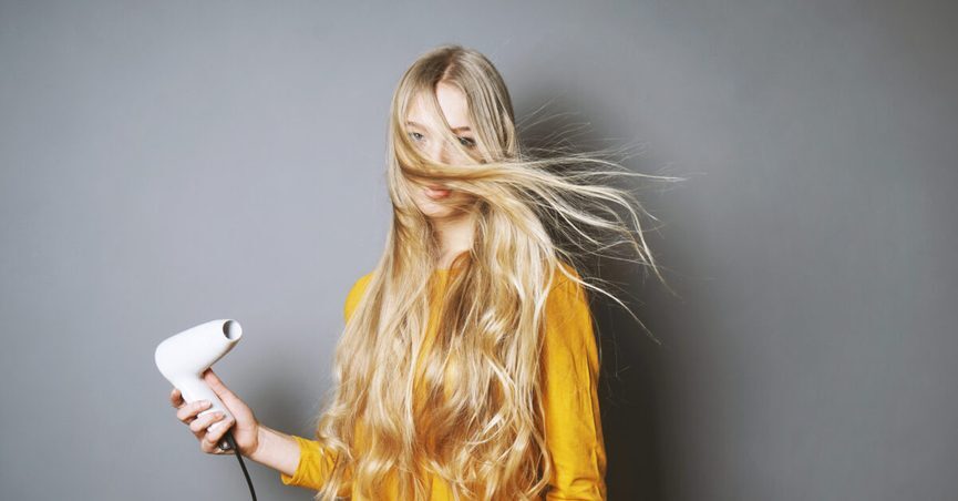 portrait-of-young-woman-blowing-hair-against-gray-background